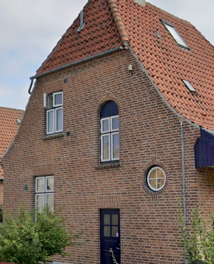 Traditional Dutch brick house with red tile roof, white-trimmed windows, dark blue door, and round porthole window